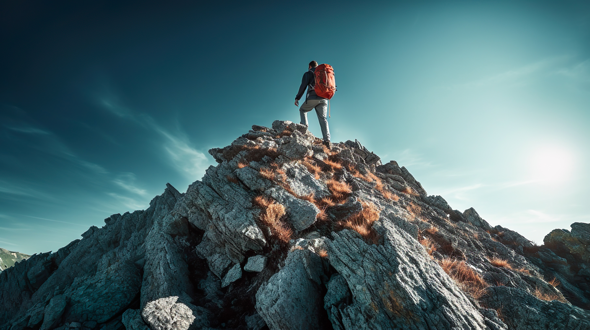 Man with a large orange backpack standing on the peak of a mountain looking into the distance